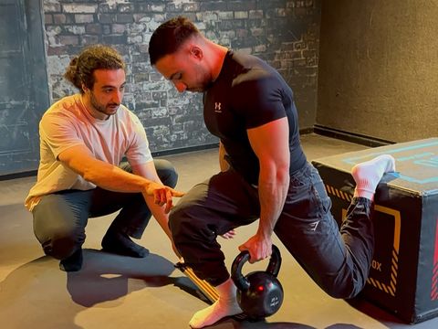 Faruk korrigiert im Studio die Technik eines Kunden bei Split Squats mit Kettlebell